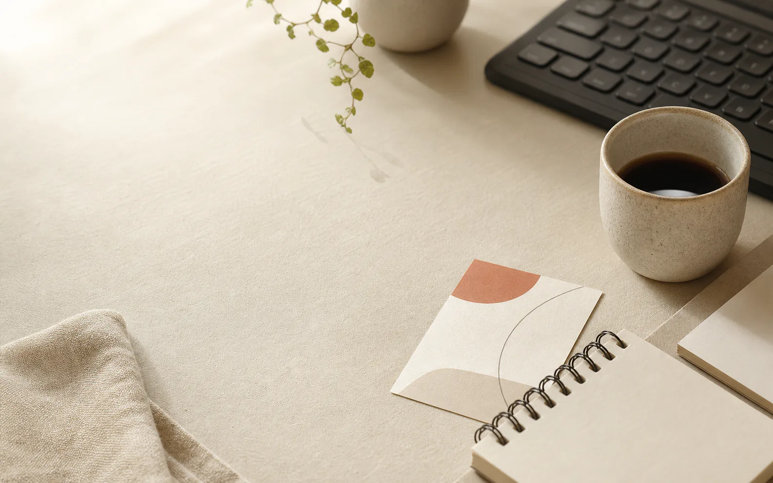 A quiet studio desk with a notebook, coffee, keyboard, and printed brand card.